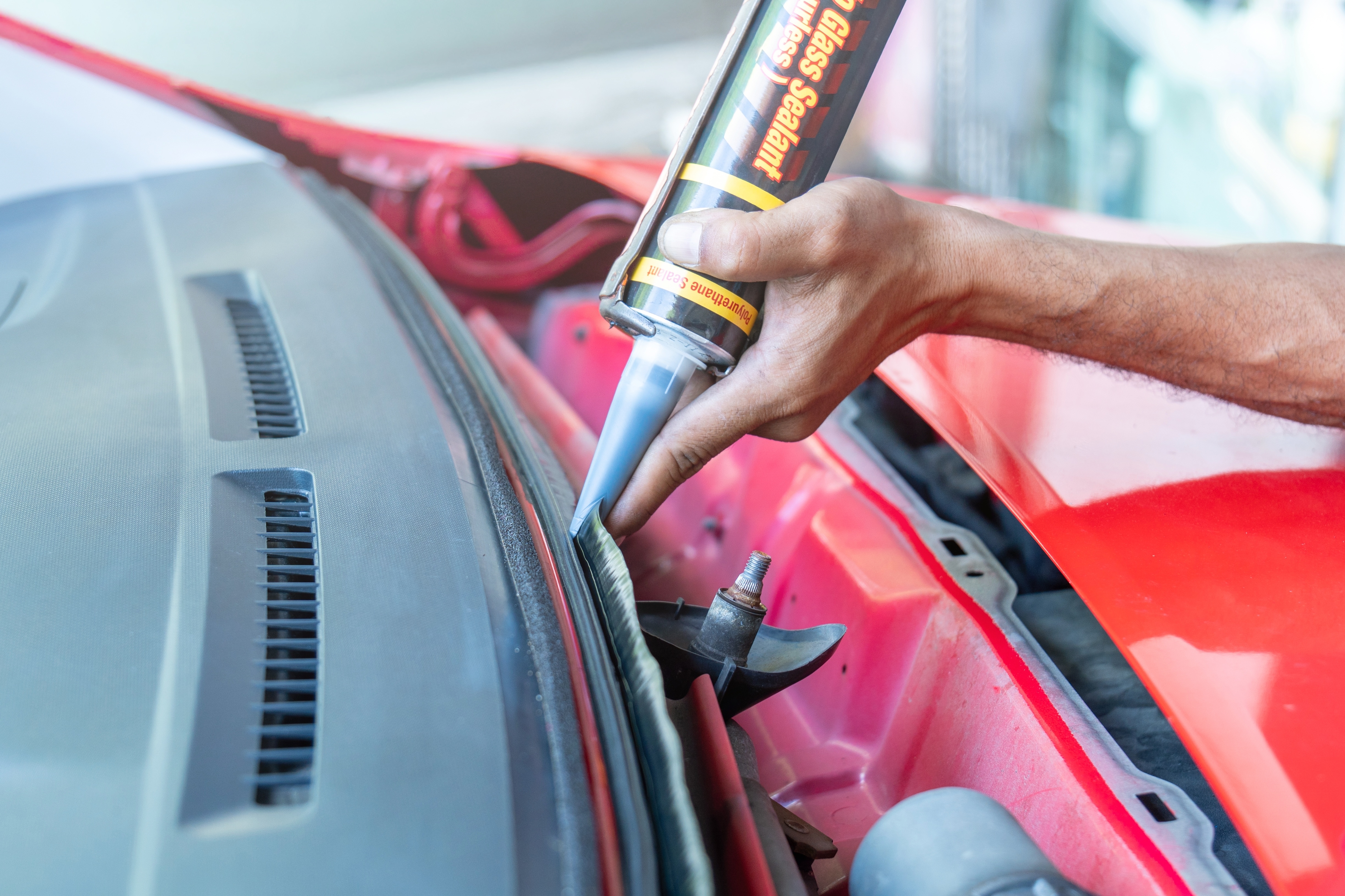 Auftragen von Dichtmasse an der Frontscheibe eines roten Fahrzeugs